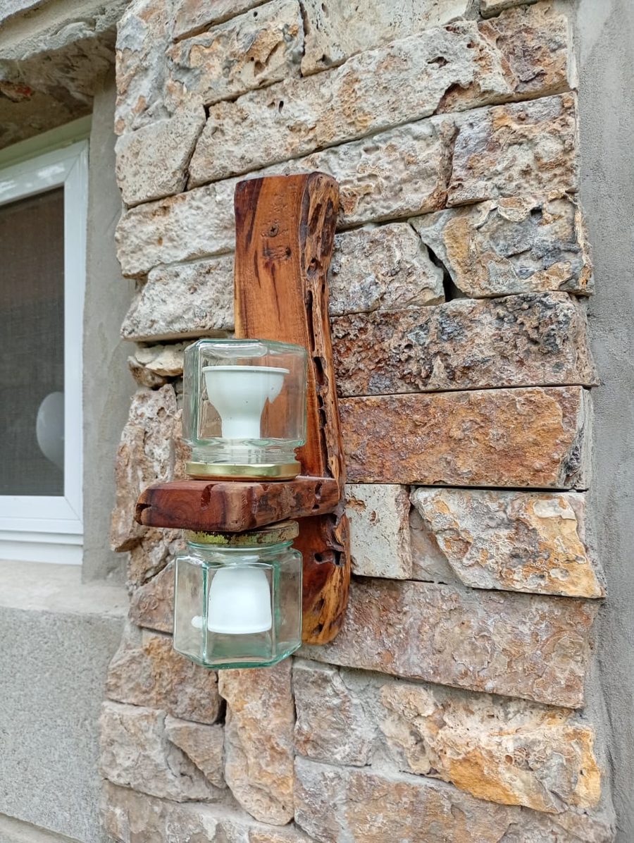 Aplique de iluminación artesanal en madera y vidrio sobre pared de piedra